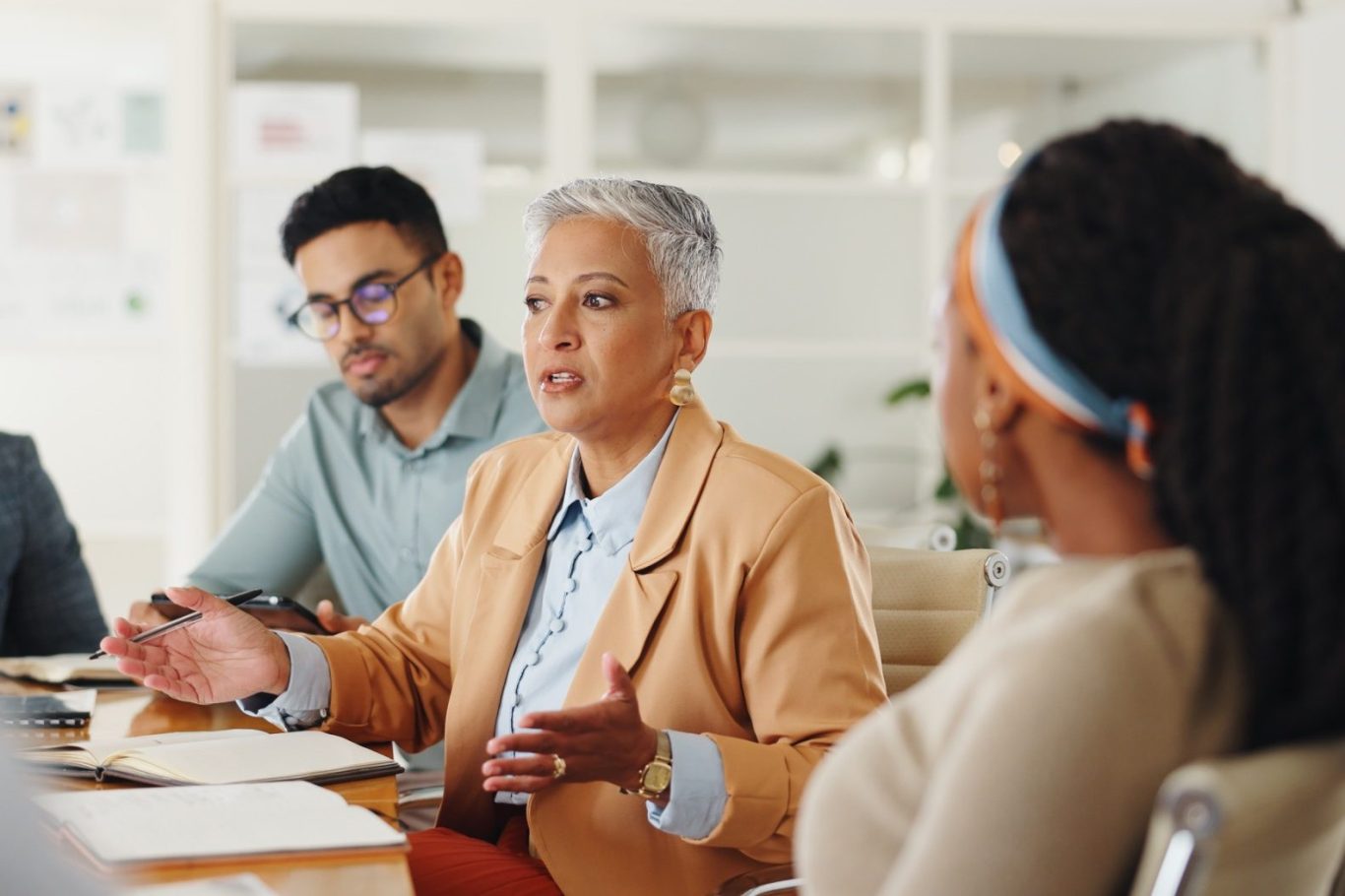 Drei Personen in einer Besprechung, eine Frau spricht, während die anderen zuhören.