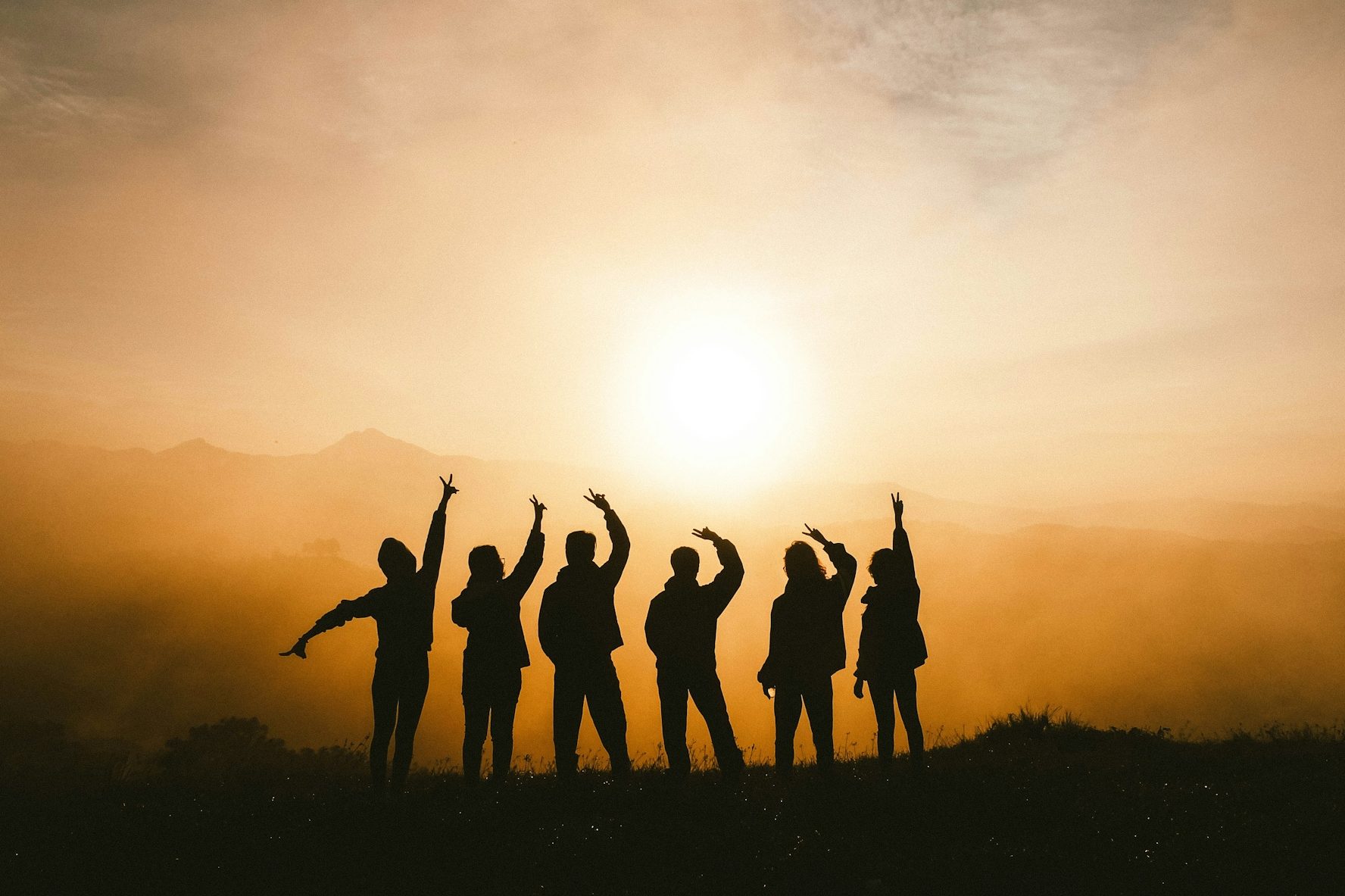 Gruppensilhouetten von Menschen bei Sonnenuntergang, Hände nach oben gestreckt.