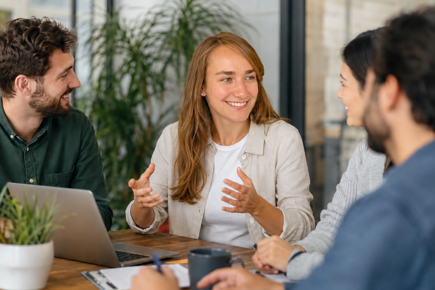 Vier Personen in Geschäftsanzügen diskutieren an einem Tisch mit Laptops und Unterlagen.